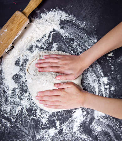 Baking preparing background. Female hands knead dough on the worktop.