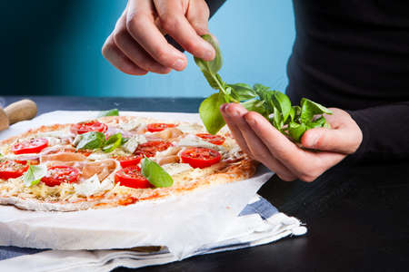 Hands of baker adding ingredients into pizza during pizza preparation at kitchen