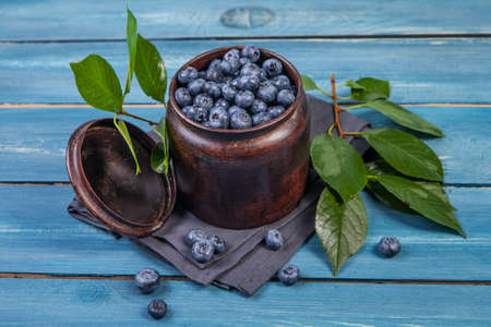 Juicy and fresh blueberries with green leaves on blue wooden table.の写真素材