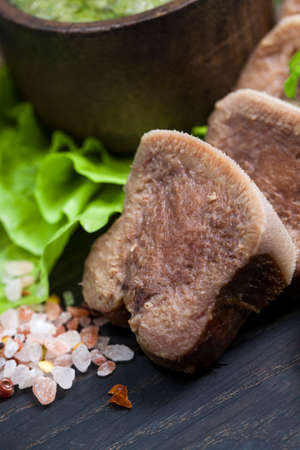 Boiled beef tongue on dark wooden table with pesto and saladの写真素材