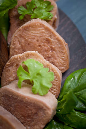 Boiled beef tongue on dark wooden table with pesto and salad
