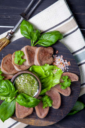 Boiled beef tongue on dark wooden table with pesto and saladの写真素材