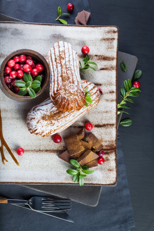Cream eclairs choux pastries served with fresh cranberries on a handmade ceramic plateの写真素材