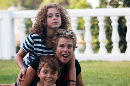 Happy family made of a mother and her two children, a boy and a girl photographed in a garden during the summerの写真素材