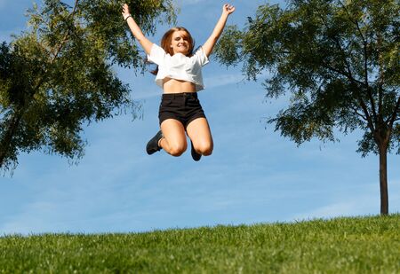 Young girl giving a joy jump in the green field with the blue sky behind herの写真素材