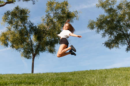 Young girl giving a joy jump in the green field with the blue sky behind herの写真素材