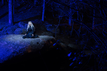 Portrait of a woman on a large rock in the dark and illuminated with coloured lanternsの写真素材