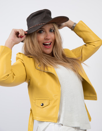 Woman with blonde hair and blue eyes with yellow jacket, poses in photographic studio with white background.の写真素材
