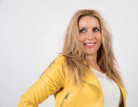 Woman with blonde hair and blue eyes with yellow jacket, poses in photographic studio with white background.の写真素材