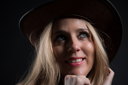 Woman with blonde hair and blue eyes dressed in dark color and with her head covered, she poses in a photographic studio with black background.の写真素材