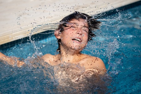 12 year old boy playing in the swimming pool of his house during the summer.