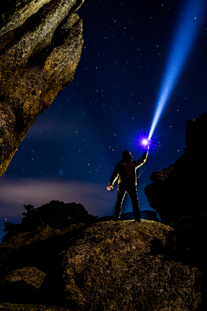 Man on a rock illuminating the dark night sky with a very powerful flashlightの写真素材
