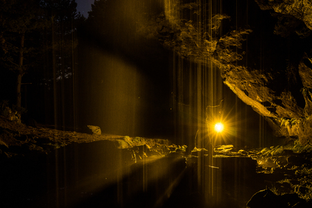 Night photograph inside a cave with waterfall and illuminated with coloured lanterns to highlight the figure of the model.の写真素材