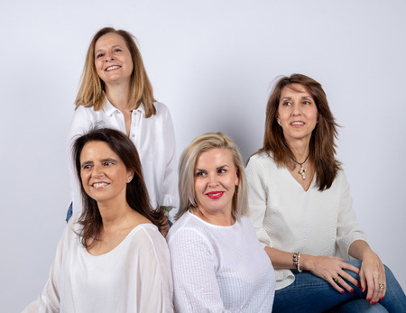 Group of 4 women, friends, middle-aged having fun in a photo session in a studio with white background, sitting on a ballの写真素材