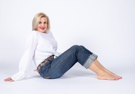 Photographic studio session for a 50 year old woman sitting on the floor and dressed in jeans and white shirt.の写真素材