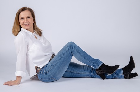Photographic studio session for a 50 year old woman sitting on the floor and dressed in jeans and white shirt.の写真素材