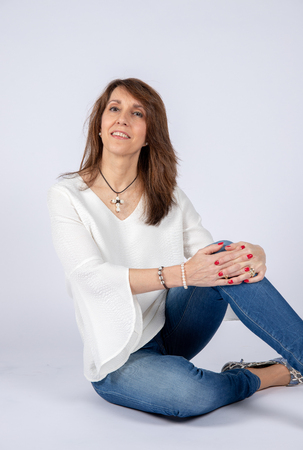 Photographic studio session for a 50 year old woman sitting on the floor and dressed in jeans and white shirt.の写真素材