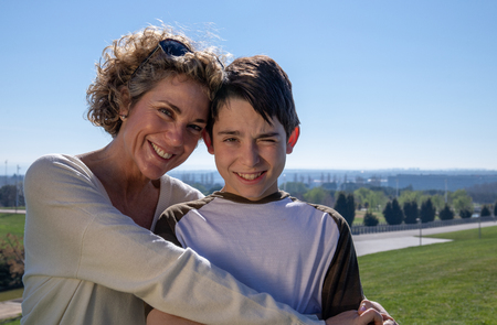 Mother with her 12 year old son in a loving attitude on a summer day in a public park.の写真素材