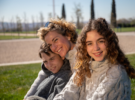 Family made up of a mother, son and daughter pose on a sunny day in a public park with a very affectionate attitude.の写真素材