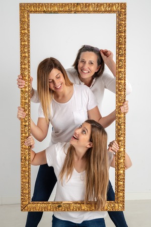 Family composed by mother and two twin sisters pose inside a pictorial frame in a photographic studio and in a very funny attitude.の写真素材