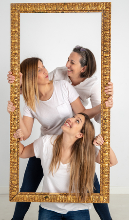 Family composed by mother and two twin sisters pose inside a pictorial frame in a photographic...
