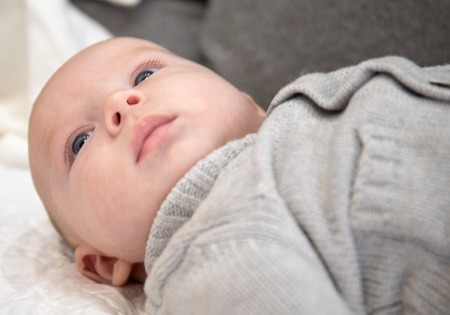Baby lying in bed and in a grey sweater looks carefully at his parents out of the planeの写真素材