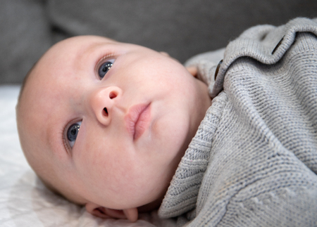 Baby lying in bed and in a grey sweater looks carefully at his parents out of the planeの写真素材