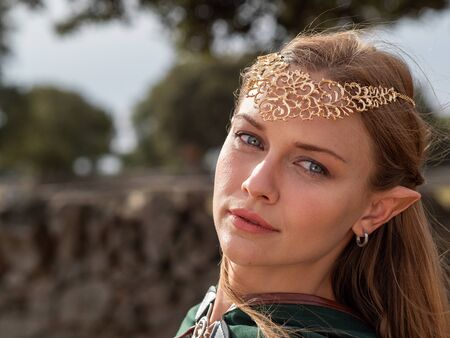 Close-up of blonde woman with blue eyes and elf ears in the field wearing a green capeの写真素材