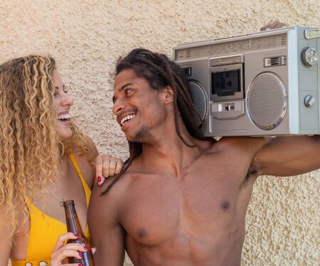 Caucasian blonde girl and black boy with dreadlocks, they hear music on a vintage stereo cassette radio.の写真素材