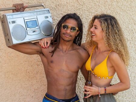 Caucasian blonde girl and black boy with dreadlocks, they dance with an antique stereo and wear sunglasses.の写真素材