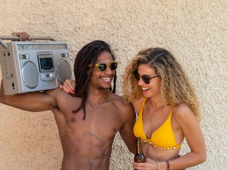 Caucasian blonde girl and black boy with dreadlocks, they dance with an antique stereo and wear sunglasses.の写真素材