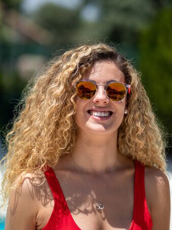 Blonde girl with curly hair and red swimsuit front sight with sunglassesの写真素材