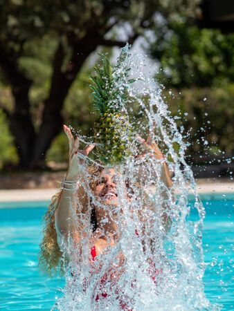 Caucasian blonde girl plays with a pineapple in the poolの写真素材