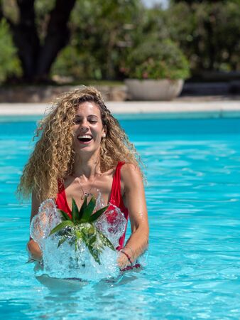 Caucasian blonde girl plays with a pineapple in the poolの写真素材