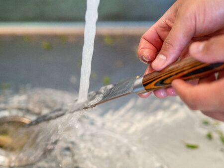 Man's hands washing under the tap a kitchen knifeの写真素材