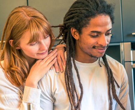 Interracial couple formed by African and Caucasian prepare a salad together with the help of their cell phoneの写真素材