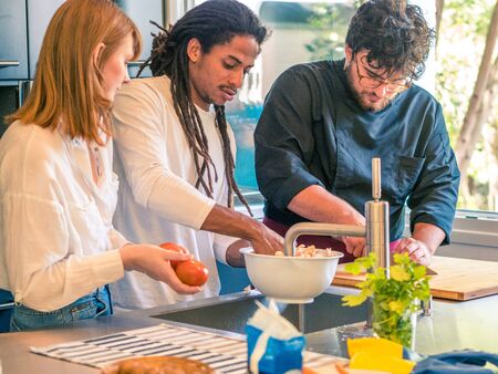 Interracial couple of African husband and Caucasian wife prepare food together with a professional chefの写真素材