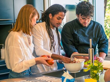Interracial couple of African husband and Caucasian wife prepare food together with a professional chefの写真素材