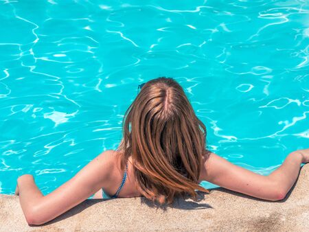 Caucasian girl with red hair, poses with her back moving her hair and with a blue bathing suit