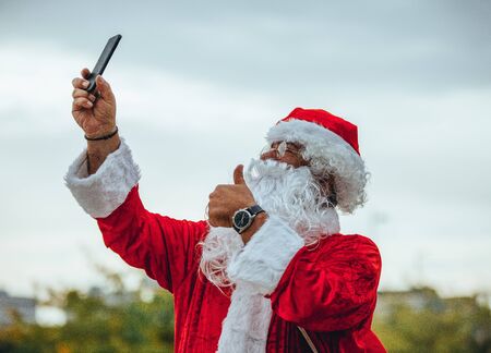Stock photo of Santa Claus making a selfie with the mobile in one hand and the other making the symbol of victory. Christmas timeの写真素材