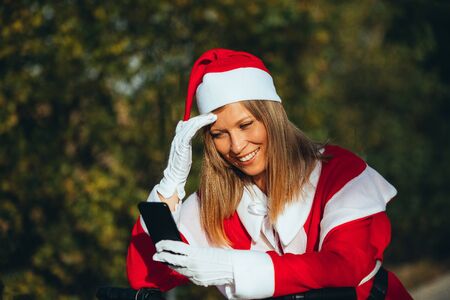 Stock photo of Mama noel looking at the mobile resting on the handlebars of the bicycle with expression of happiness. Christmas timeの写真素材