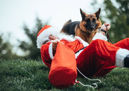 Stock photo of Santa claus sitting on the lawn, playing with his dog. Christmas time and Noelの写真素材