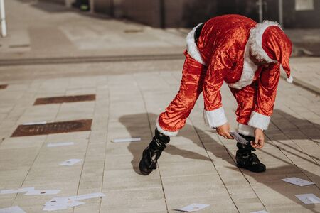 Stock photo of Santa claus without beard in the street watching as the children's letters fly in the air with a red bag on the table. Christmas timeの写真素材