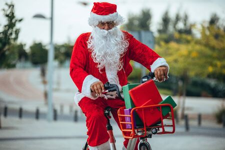 Stock photo of Santa Claus with gifts in the bicycle and his red suitcase on his back. Christmas timeの写真素材
