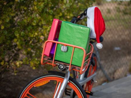 Stock photo of orange bicycle with basket on the front, loaded with gifts and a Santa Claus cap attached to the handlebars. Christmas timeの写真素材