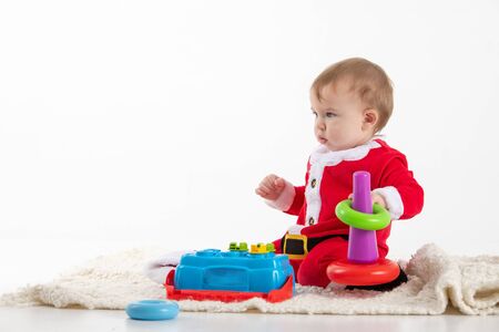 Stock studio photo with white background with a baby dressed as Santa Claus sitting on the floor playing with toys.の写真素材