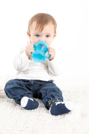 Stock studio photo with a white background of a baby drinking water from a canteen with handles.の写真素材