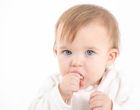 Stock studio photo with the white background of a baby's face with the hand in the mouthの写真素材