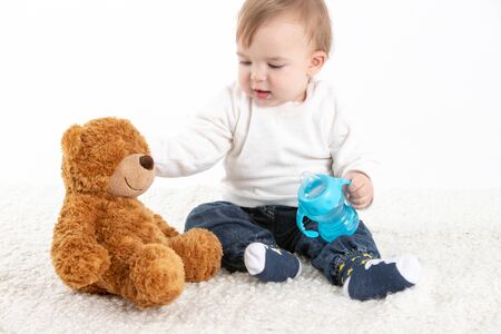 Stock studio photo with a white background of a baby sitting with a canteen with handles and a teddy bear.の写真素材