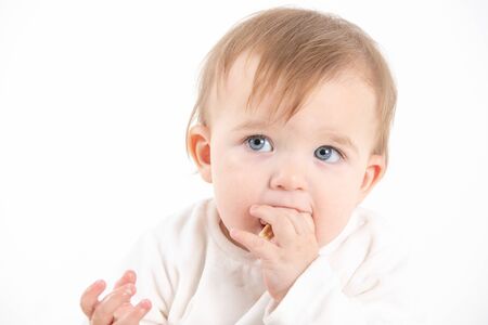 Stock studio photo with the white background of a baby's face with fingers in the mouthの写真素材